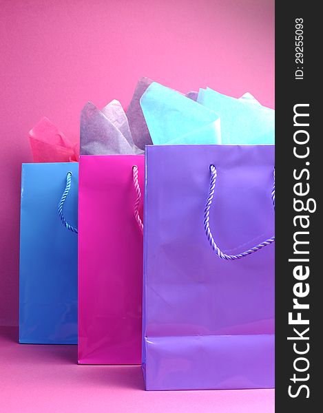 Retail therapy, I love shopping, concept with colorful pink, blue and purple shopping bags against a pink background, vertical side view. Retail therapy, I love shopping, concept with colorful pink, blue and purple shopping bags against a pink background, vertical side view.
