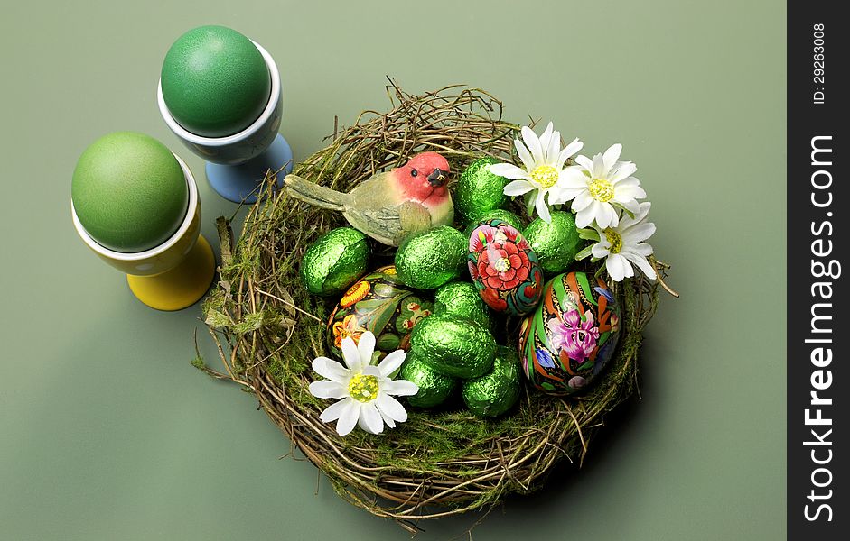 Happy Easter nest of chocolate and hand painted eggs, bird and daisies on a green table setting. Happy Easter nest of chocolate and hand painted eggs, bird and daisies on a green table setting.