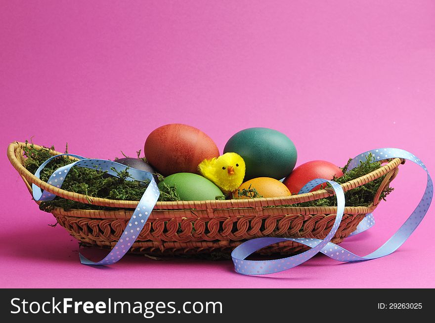 Rainbow color easter eggs on grass in wicker basket with blue polka dot ribbon against a pink background. Rainbow color easter eggs on grass in wicker basket with blue polka dot ribbon against a pink background.