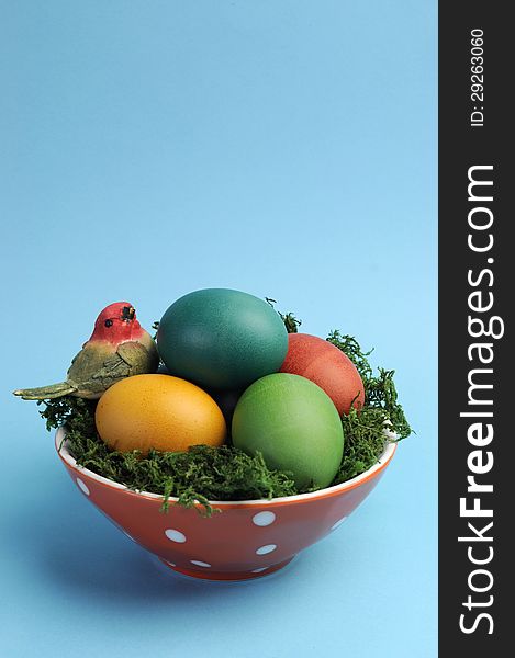 Bright and cheerful Happy Easter still life with rainbow color eggs in orange polka dot bowl against a blue background.