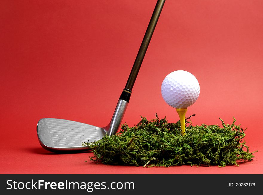 Sporting and Leisure pursuit, golf club iron, yellow tee with white golf ball on grass against  a red background, with copy space. Sporting and Leisure pursuit, golf club iron, yellow tee with white golf ball on grass against  a red background, with copy space.