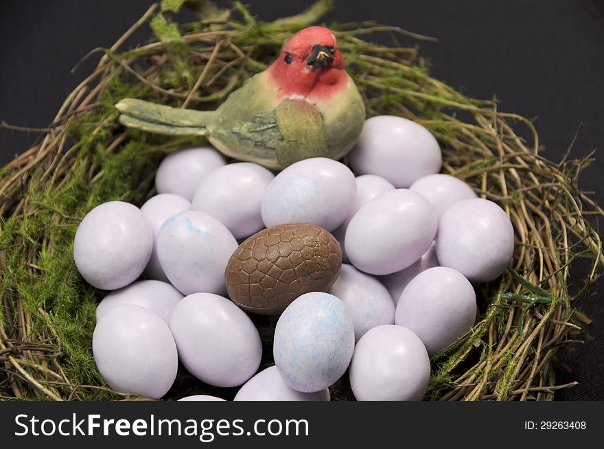 Close-up of chocolate Easter egg among sugar coated candy marble eggs in moss birds nest against a black background.