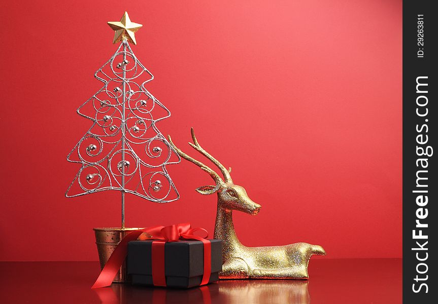 Silver and gold glitter Christmas tree and reindeer ornaments with black and red present gift still life against a festive holiday red background. Silver and gold glitter Christmas tree and reindeer ornaments with black and red present gift still life against a festive holiday red background.