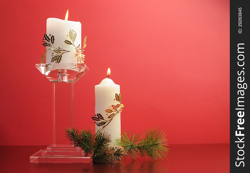 Lit white Christmas candles with festive holiday gold decoration and pine branches still life against a festive holiday red background.