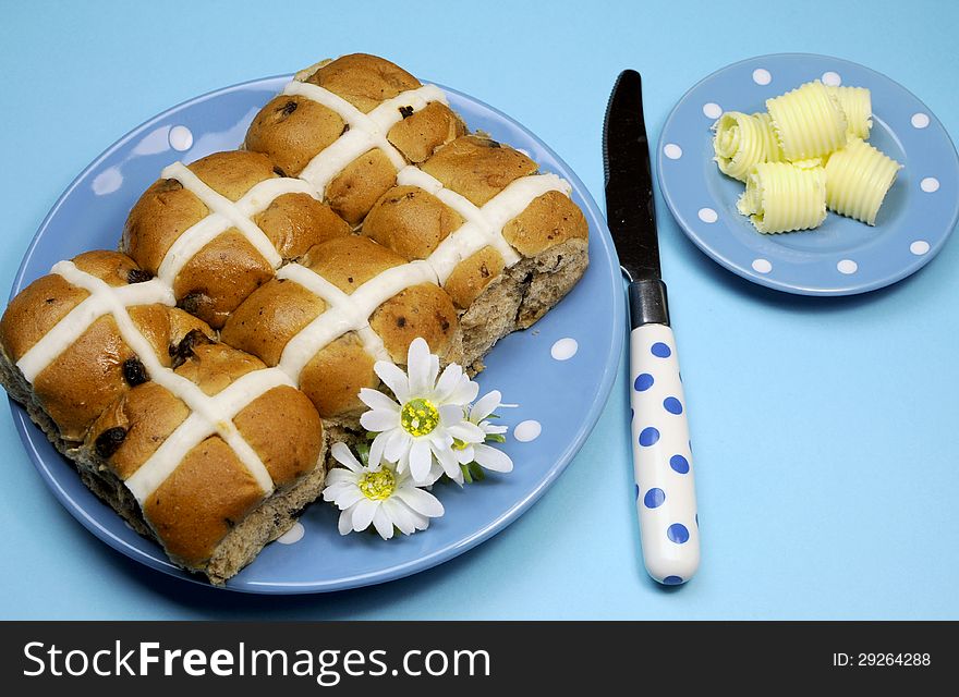 Traditional Australian and English Easter Good Friday meal, Hot Cross Buns, on blue polka dot plate with knife and butter curls on blue background. Traditional Australian and English Easter Good Friday meal, Hot Cross Buns, on blue polka dot plate with knife and butter curls on blue background.