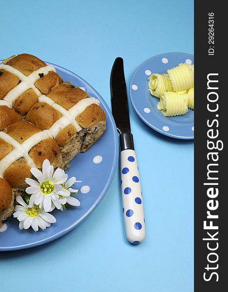 Traditional Australian and English Easter Good Friday meal, Hot Cross Buns, on blue polka dot plate with knife and butter curls on blue background. Traditional Australian and English Easter Good Friday meal, Hot Cross Buns, on blue polka dot plate with knife and butter curls on blue background.