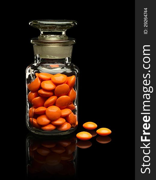 Glass vial with a glass cover and pills of orange colour on a black background. Glass vial with a glass cover and pills of orange colour on a black background