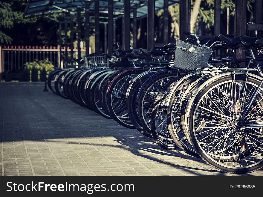 Many bicycles stand one-behind-one on the sidewalk