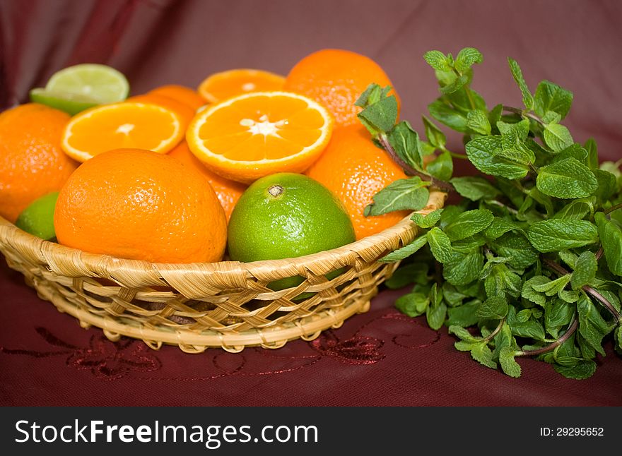 Oranges and limes in a basket with mint on a dark background