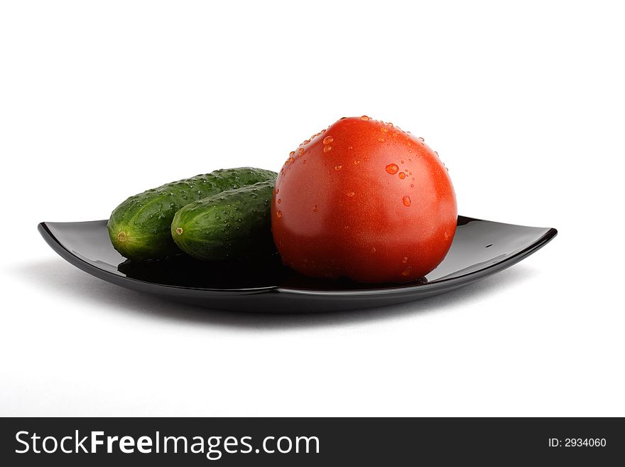 Cucumbers & tomato on a black dish. Isolated. Path.