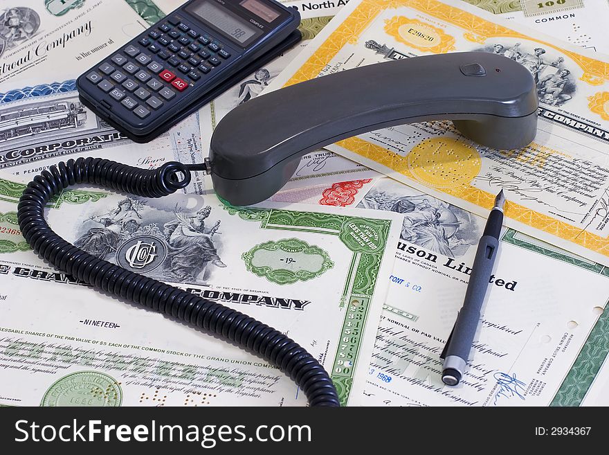 A trader board handset, calculator, and a pen on share certificates. A trader board handset, calculator, and a pen on share certificates