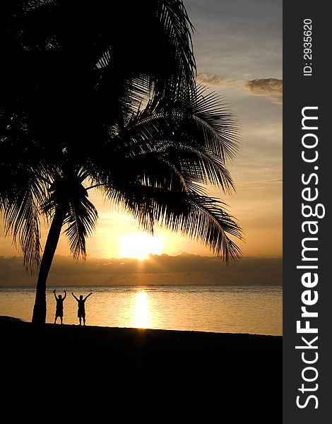 Two people raising their arms at the beach, facing the rising sun. Two people raising their arms at the beach, facing the rising sun.