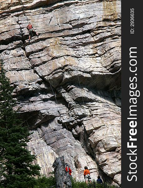A woman climbs the steep mountain as three friends work the belay lines below. A woman climbs the steep mountain as three friends work the belay lines below