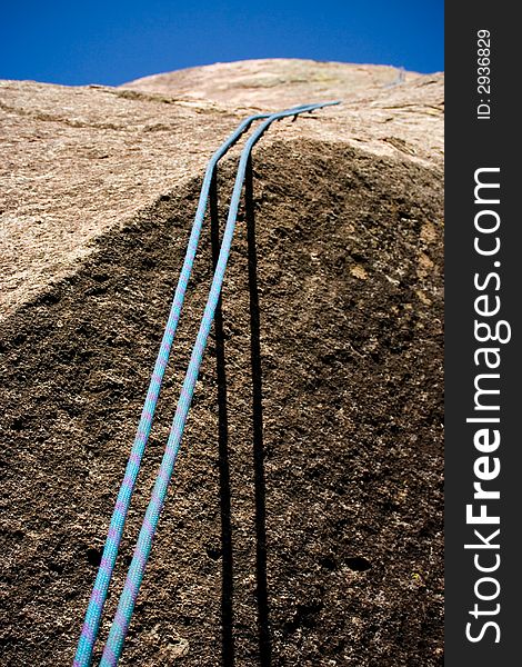 A blue dynamic climbing rope hanging stationary while waiting for a climber to bless its usage. A blue dynamic climbing rope hanging stationary while waiting for a climber to bless its usage