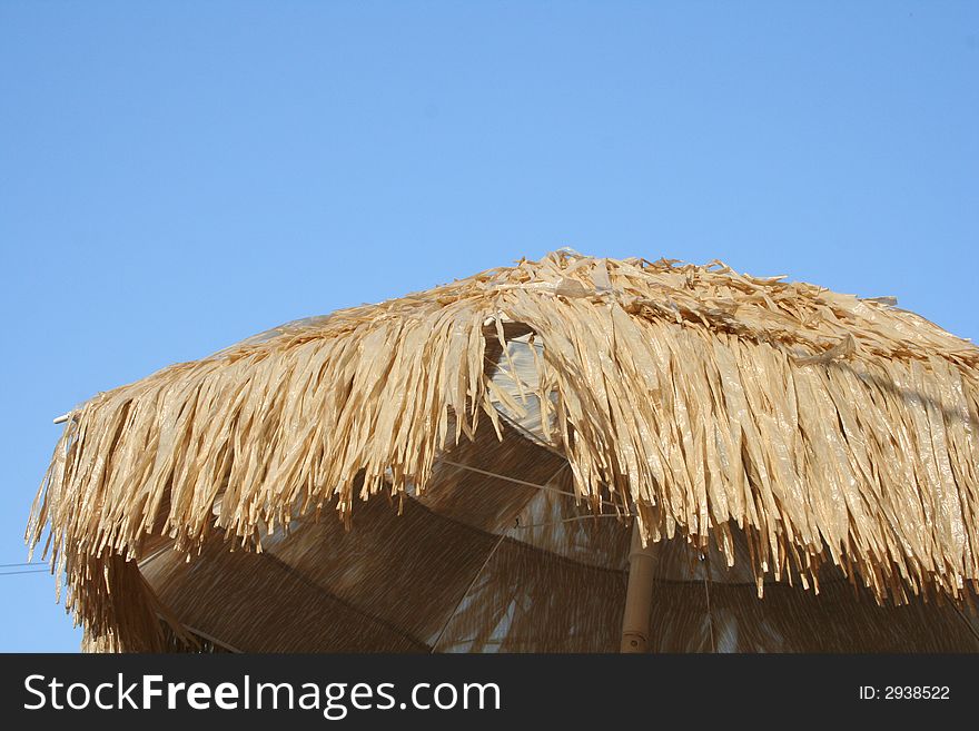 A thatched roof in a crisp blue sky.  Perfect vacation photo.