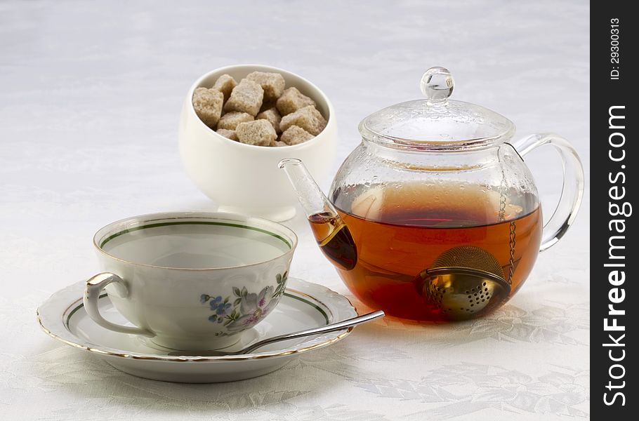 Teapot with tea, cup on a saucer and sugar bowl with brown sugar