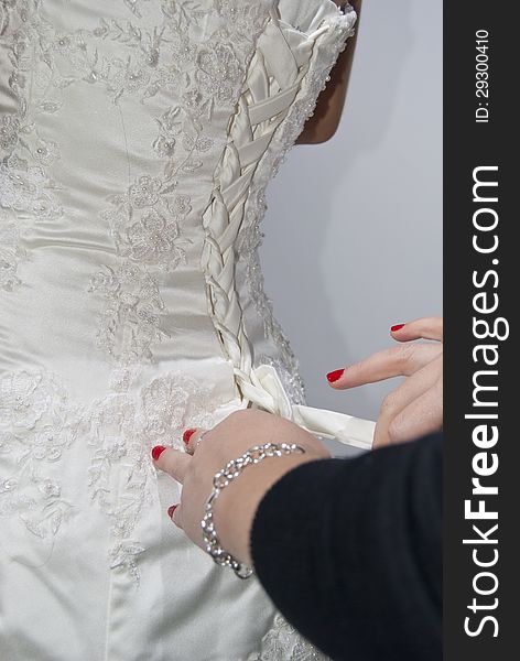 A women with bright red nails ties up the back of a wedding dress. A women with bright red nails ties up the back of a wedding dress.