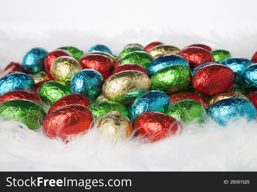 Chocolate easter eggs in colorful aluminium foil on white down. Chocolate easter eggs in colorful aluminium foil on white down