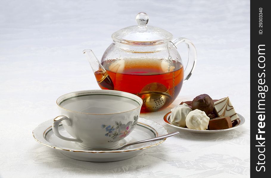 Cup on a saucer, teapot with tea and chocolates on a plate. Cup on a saucer, teapot with tea and chocolates on a plate