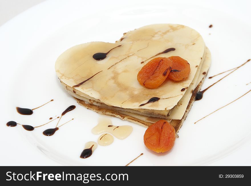 Heart-shaped pancake with dried apricots and honey on white plate. Heart-shaped pancake with dried apricots and honey on white plate