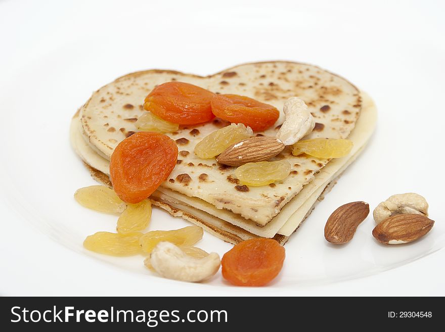 Heart-shaped pancake with dried apricots, almond, hazelnuts, cashew and raisins on white plate. Heart-shaped pancake with dried apricots, almond, hazelnuts, cashew and raisins on white plate