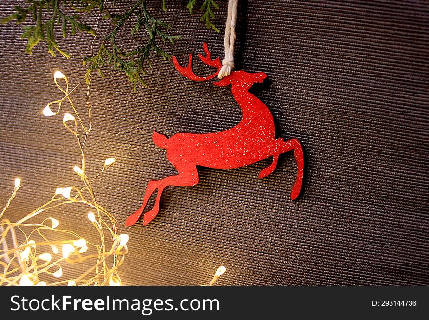 Holiday grey background with coniferous branches, light garland and a wooden figure of a red Christmas deer. Photo with empty space for text and design