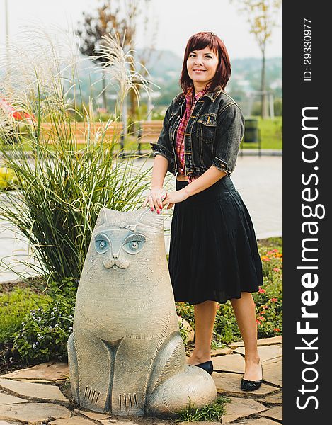 Young woman standing near funny cat statue in summer day