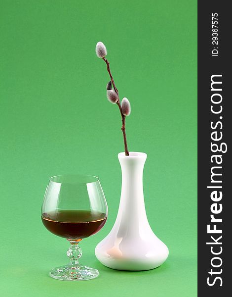 A glass of red wine and white vase with a sprig of willow. A glass of red wine and white vase with a sprig of willow