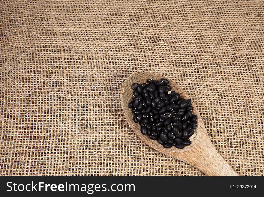 Black beans sitting on a wooden spoon on a burlap background. Black beans sitting on a wooden spoon on a burlap background