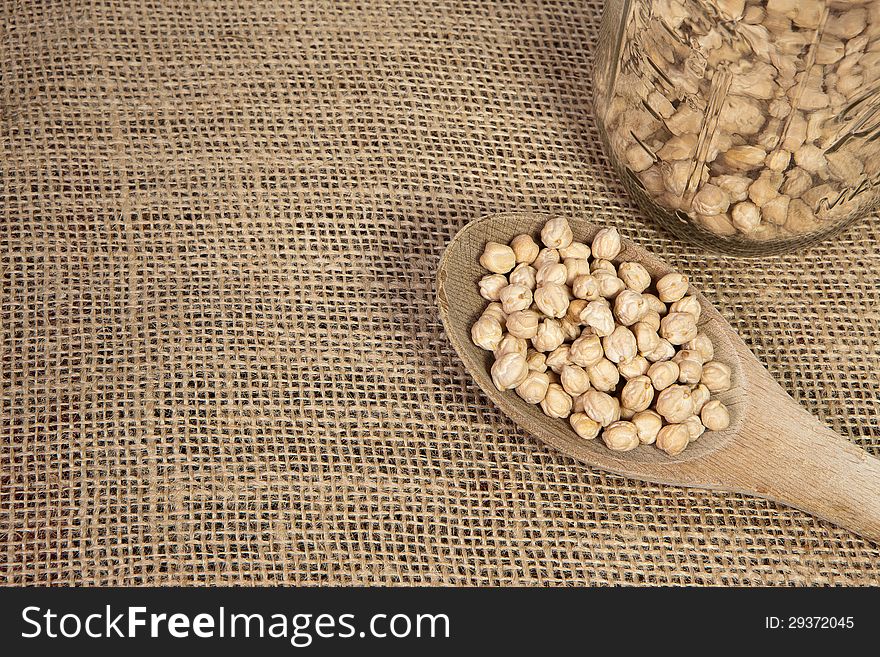 A wooden spoon with chick peas and a glass jar on a burlap background. A wooden spoon with chick peas and a glass jar on a burlap background