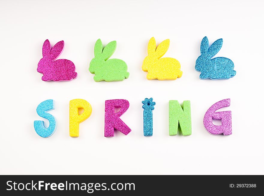 The word Spring in glitter colors of blue, yellow, purple, green. The letters are made of foam cutouts on white background. The word Spring in glitter colors of blue, yellow, purple, green. The letters are made of foam cutouts on white background.