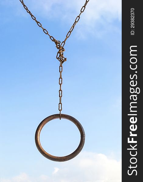 Rusty metal ring hanging on a rusty chain over blue sky