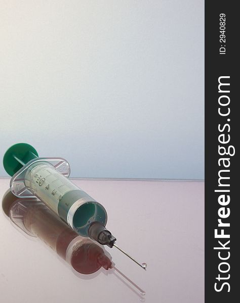 Medical syringe with a green straw on the piston and the top of the needle. It's glass, see the reflection. The background of a frosted glass. Medical syringe with a green straw on the piston and the top of the needle. It's glass, see the reflection. The background of a frosted glass.