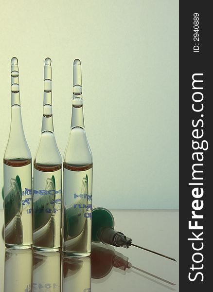 Three ampoules of drugs and a syringe lying on a glass shelf in the background mat 
glass. In ampoules are syringe. Three ampoules of drugs and a syringe lying on a glass shelf in the background mat 
glass. In ampoules are syringe.