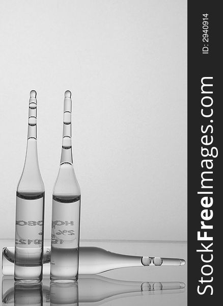 Three ampoules of drugs based on a glass shelf in the background mat glass. Photo black and white. Three ampoules of drugs based on a glass shelf in the background mat glass. Photo black and white.