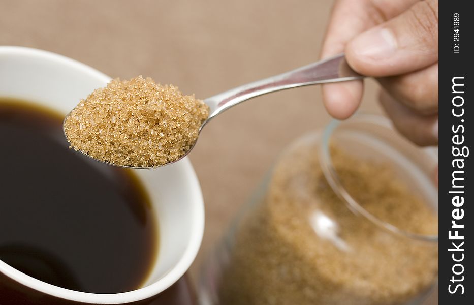 A teaspoon of brown sugar being putted into a cup of freshly brewed coffee. A teaspoon of brown sugar being putted into a cup of freshly brewed coffee
