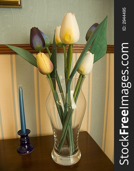 Fresh tulips in the vase on the table with the candle.