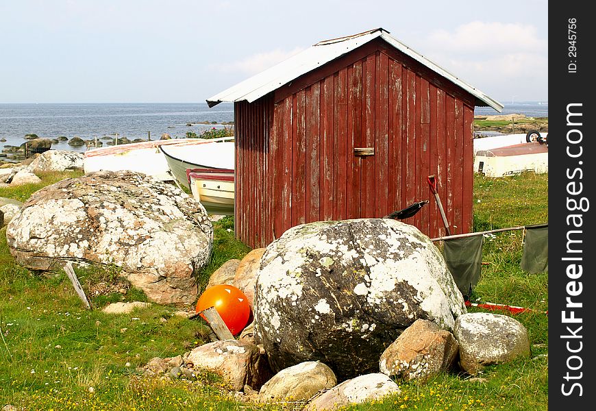 Small red boathouse with some rocks and boats around it.