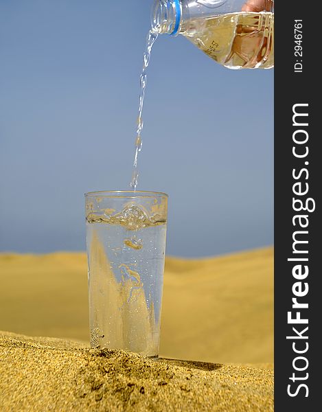 A glass of fresh water and bottle in a desert. Note that the water and bubbles are in motion blur. A glass of fresh water and bottle in a desert. Note that the water and bubbles are in motion blur.