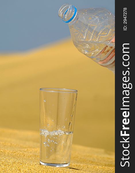 A glass of fresh water and bottle in a desert. Note that the water and bubbles are in motion blur. A glass of fresh water and bottle in a desert. Note that the water and bubbles are in motion blur.