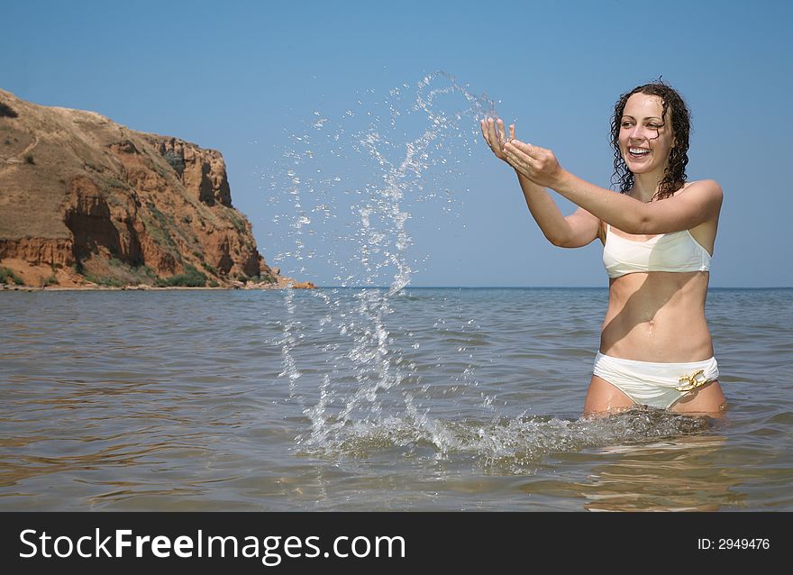 Young woman in sea sprinkles by water