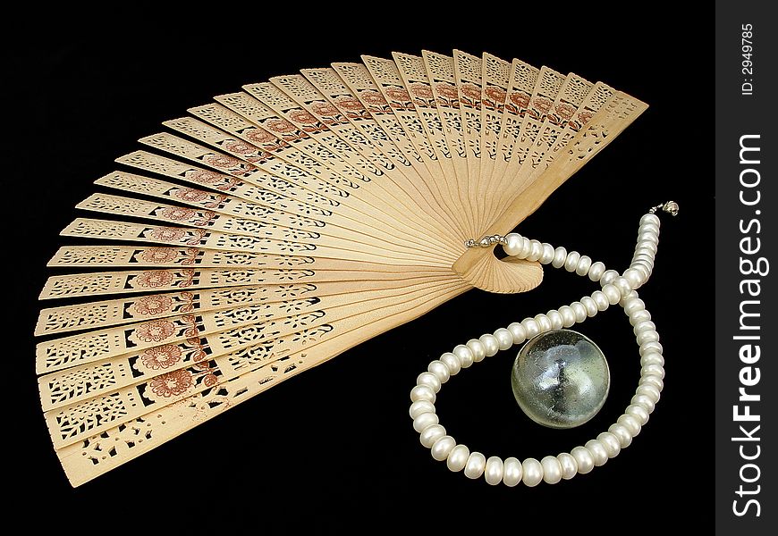 Wooden chinese fan, pearl necklace and glass nacreous sphere on the black velour. Wooden chinese fan, pearl necklace and glass nacreous sphere on the black velour