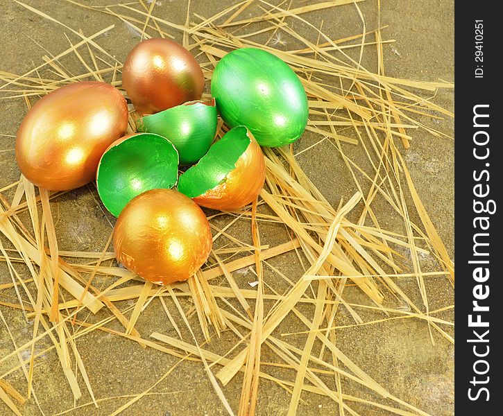 Gold Easter eggs with eggshell and straw on the sand background. Gold Easter eggs with eggshell and straw on the sand background