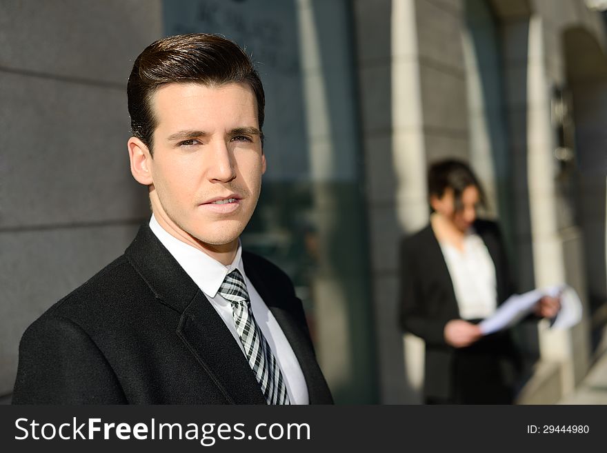 Portrait of attractive young businessman in the city with beautiful businesswoman in the background. Portrait of attractive young businessman in the city with beautiful businesswoman in the background