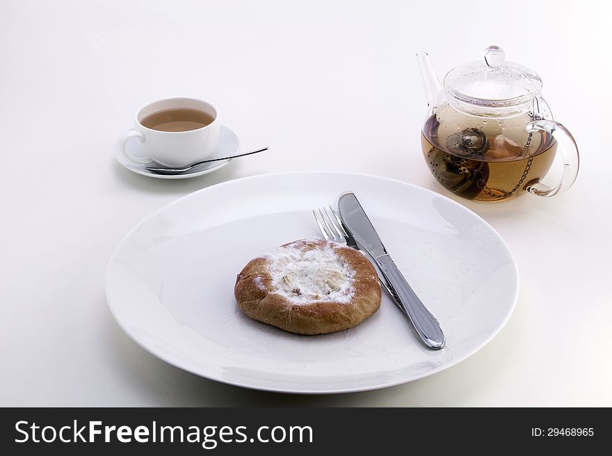 Cheese cake on a white dish, a cup with tea and a transparent teapot. Cheese cake on a white dish, a cup with tea and a transparent teapot