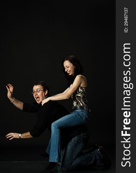 Funny young couple play in studio on black background