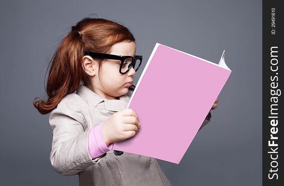 Little girl with big glasses reading a pink book. Little girl with big glasses reading a pink book