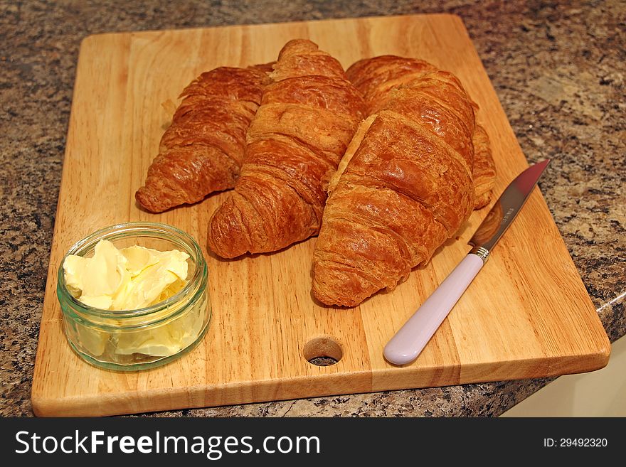 Photo showing delicious croissants on board with butter and knife. Photo showing delicious croissants on board with butter and knife.