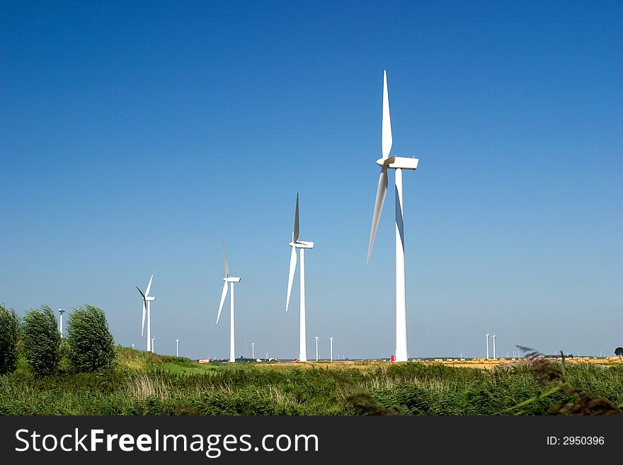 Wind turbines lined up in a field, against a clear blue sky