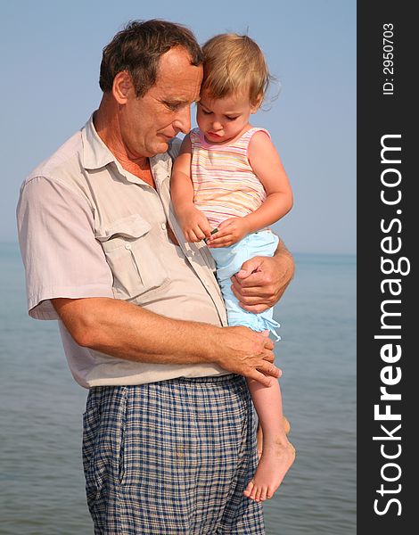 Grandfather holds granddaughter on hands at sea. Grandfather holds granddaughter on hands at sea